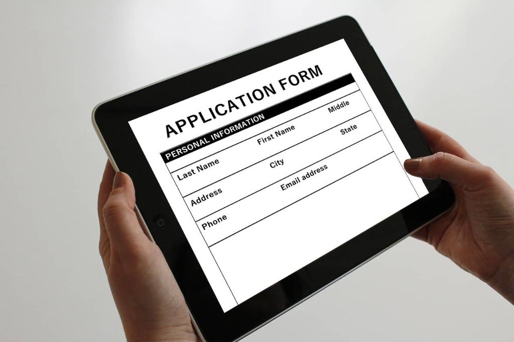 Hands holding a tablet displaying a digital application form
